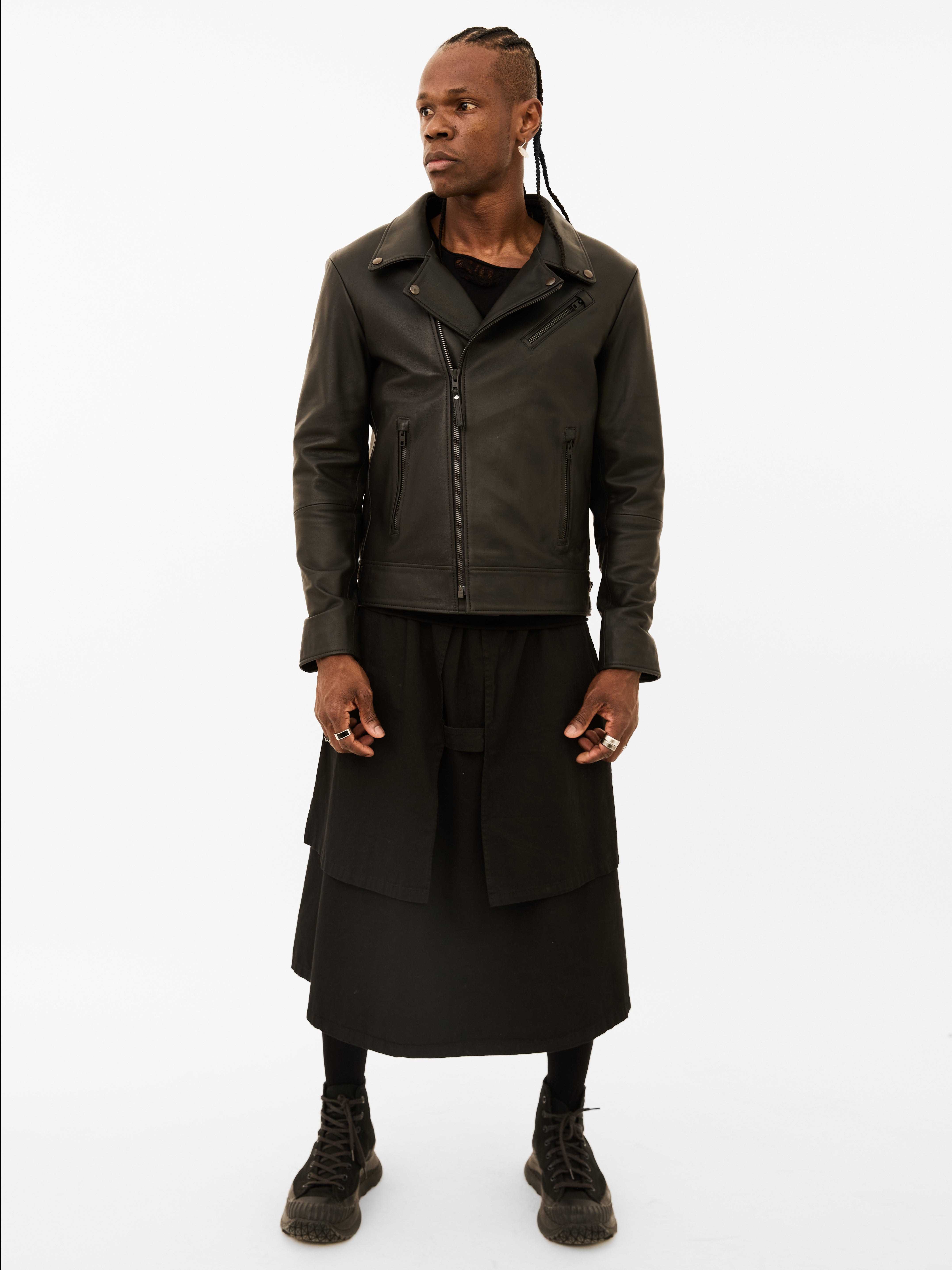 Person wearing a matta black leather biker jacket and black skirt on a white background