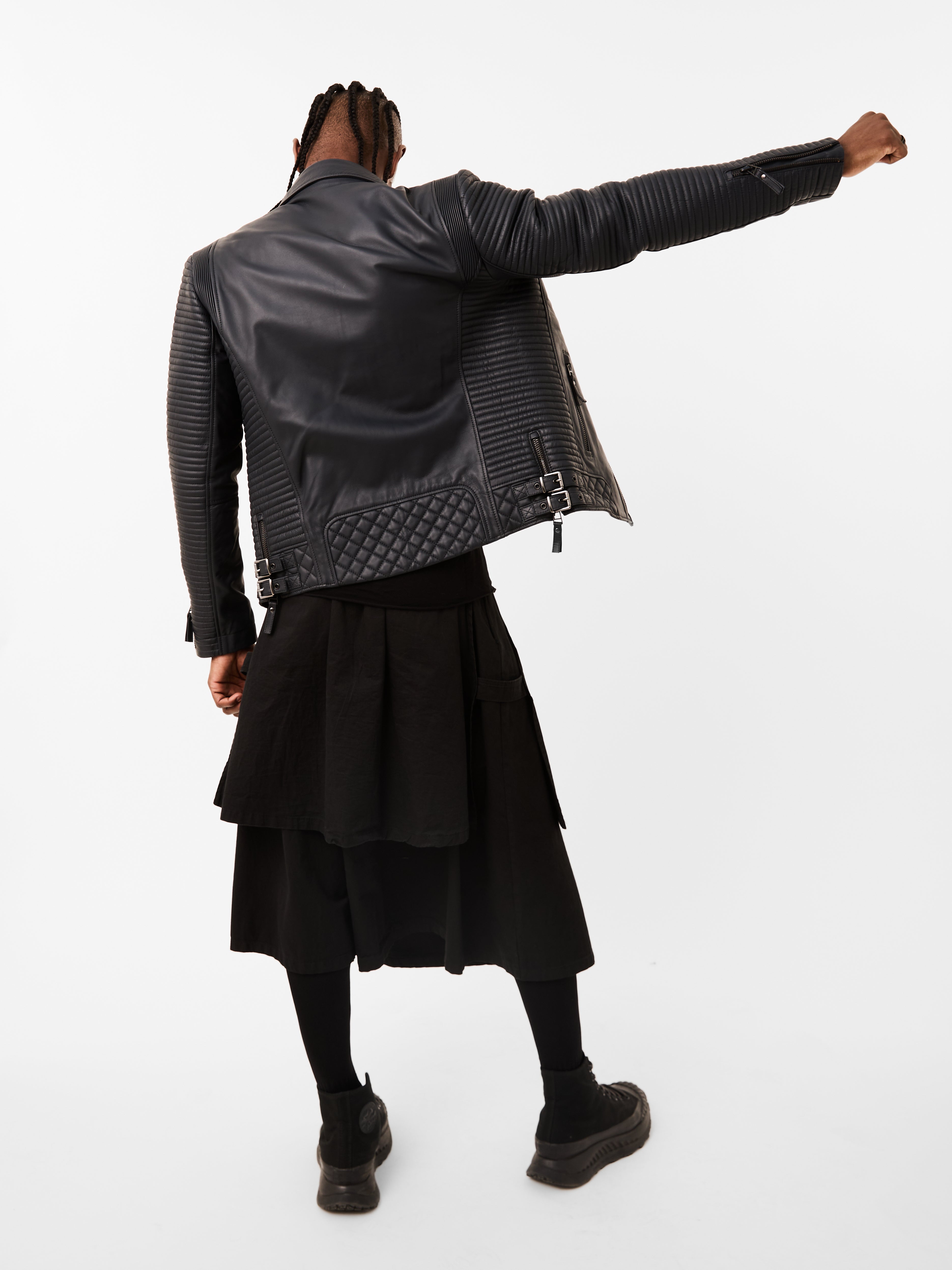 Person wearing a navy blue leather biker jacket and black skirt on a white background