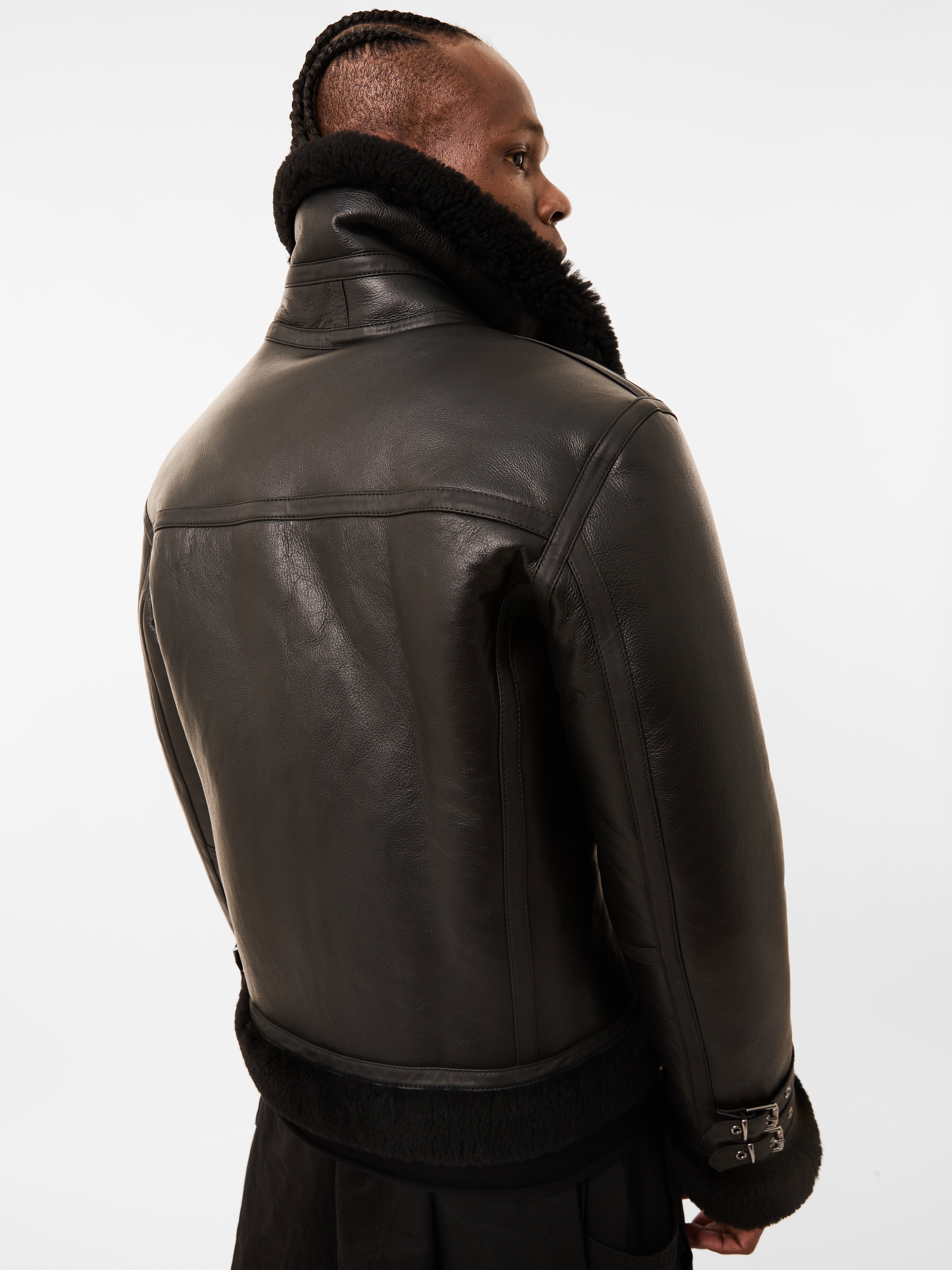 Person wearing a black leather jacket with fur collar on a white background