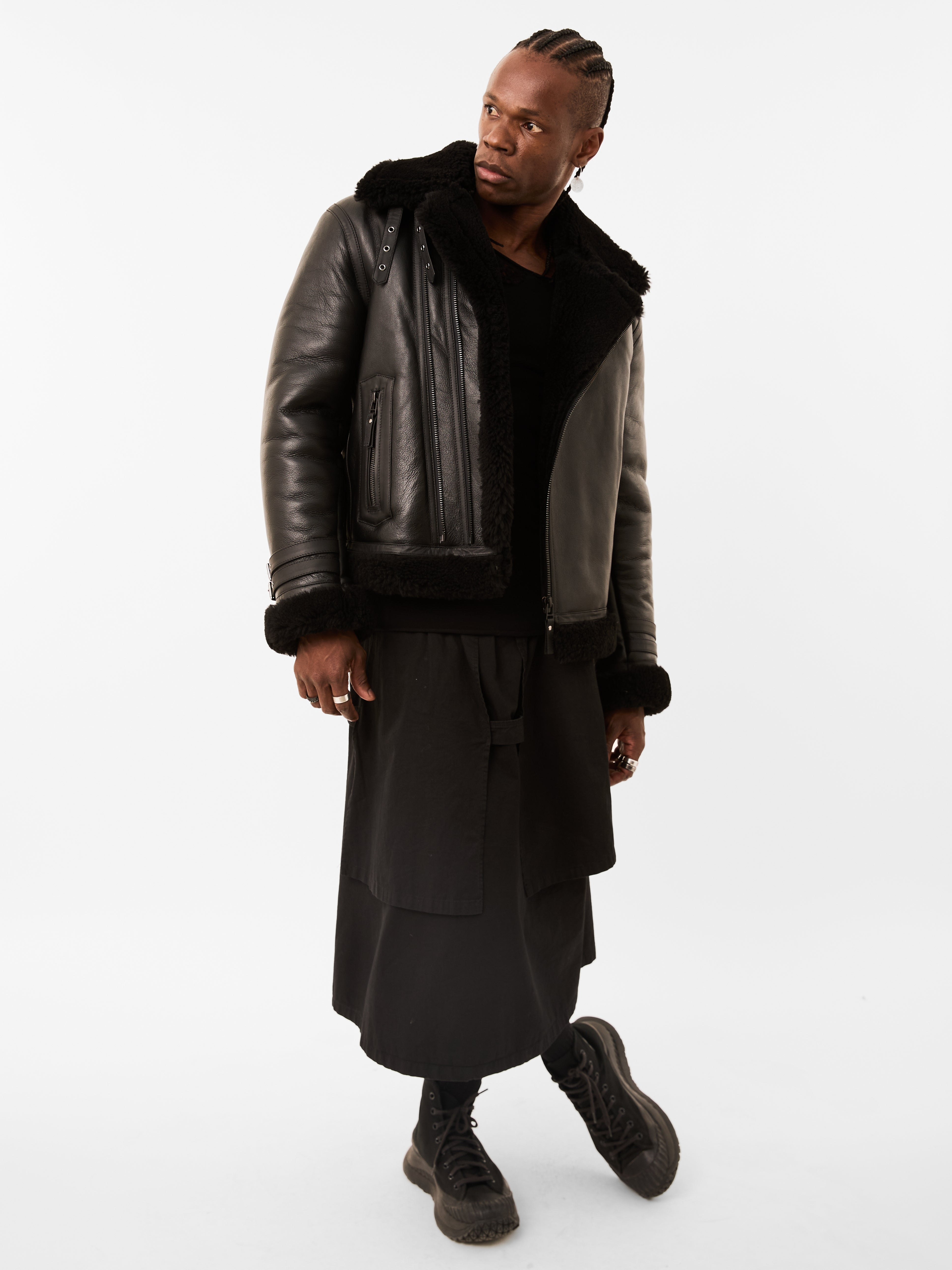 Person wearing a black leather jacket with fur trim on a white background