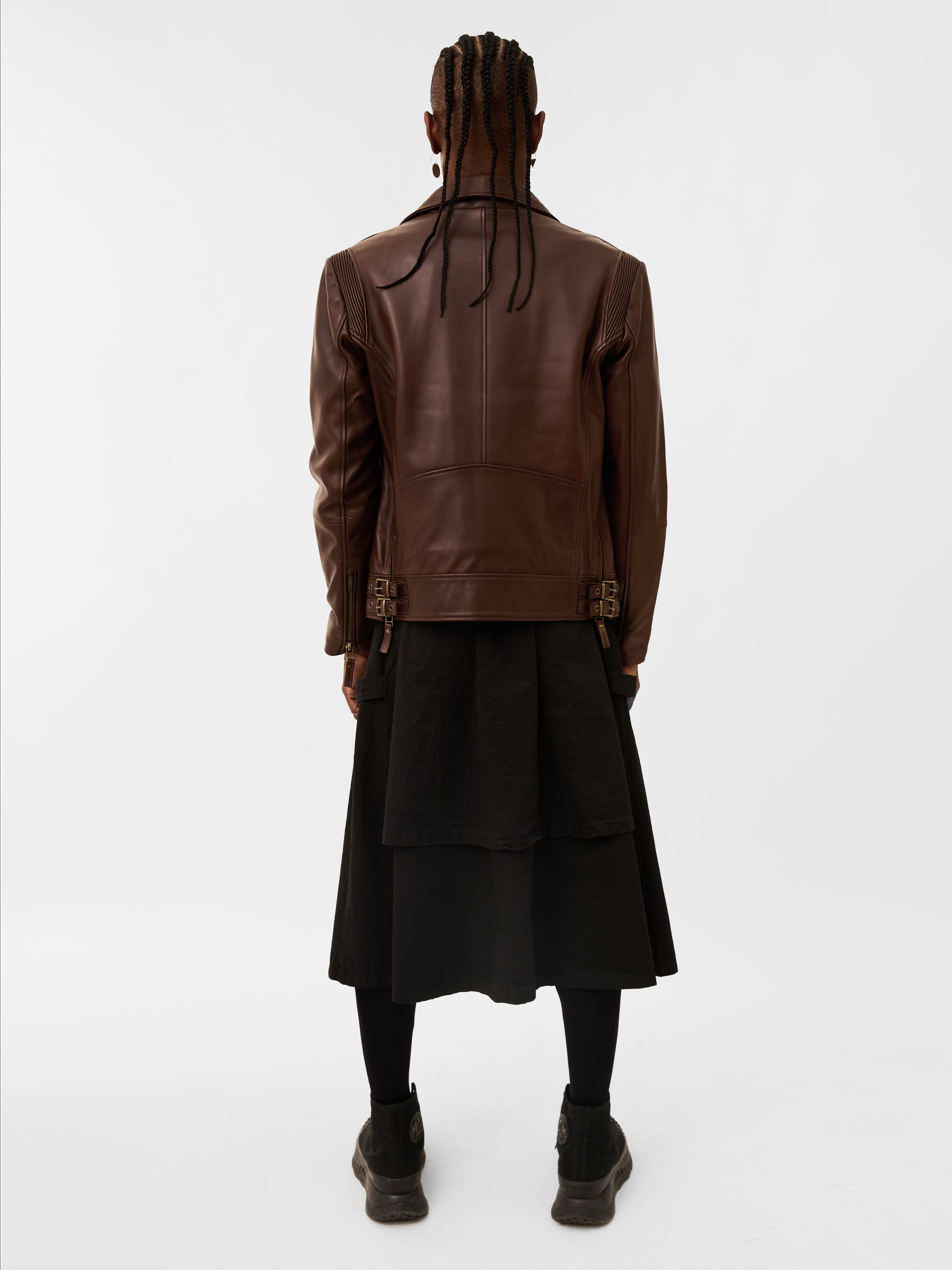 Back look of a person wearing a brown leather jacket and black skirt on a white background