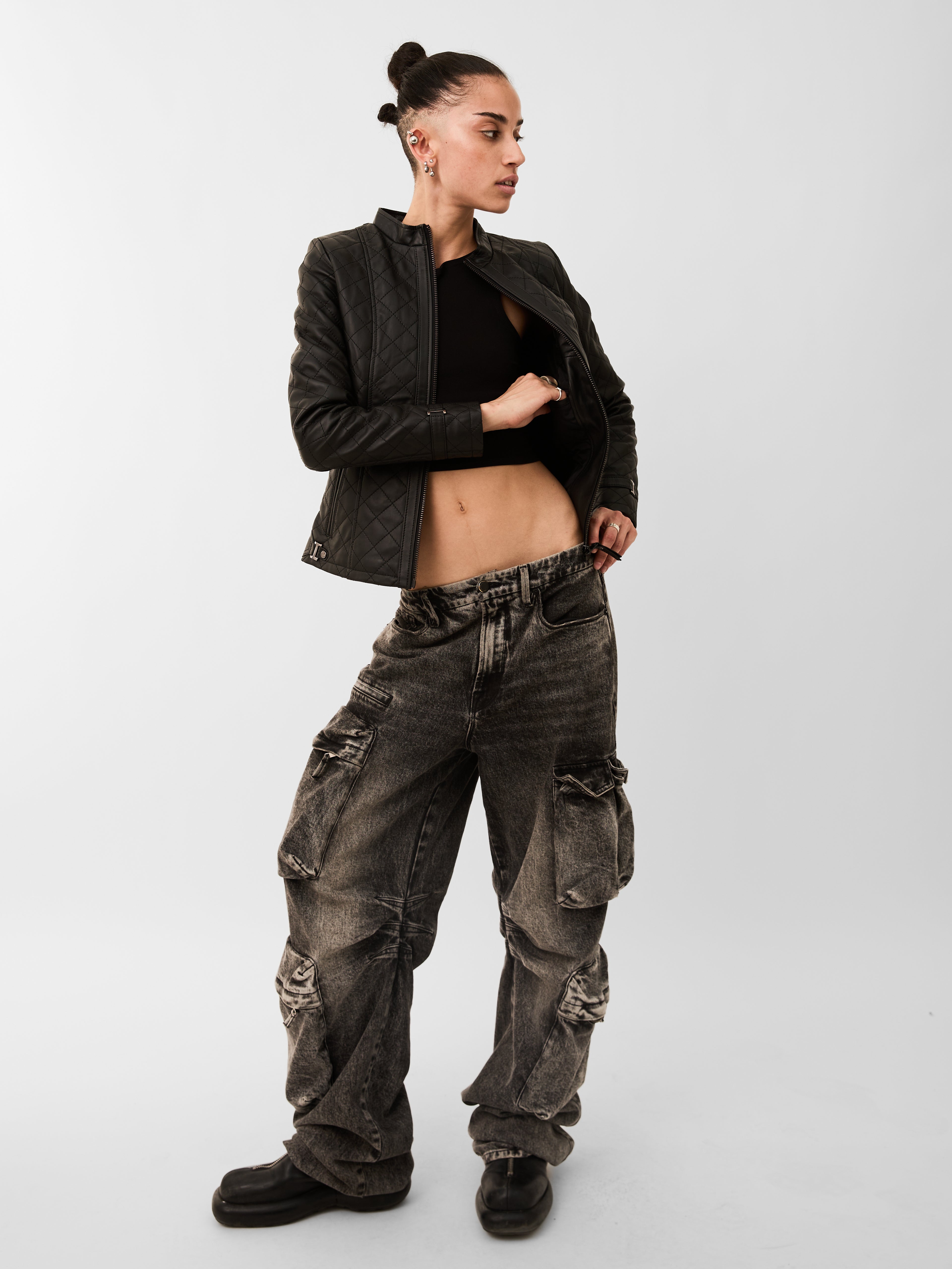 Person wearing a black leather jacket and dark cargo pants on a white background