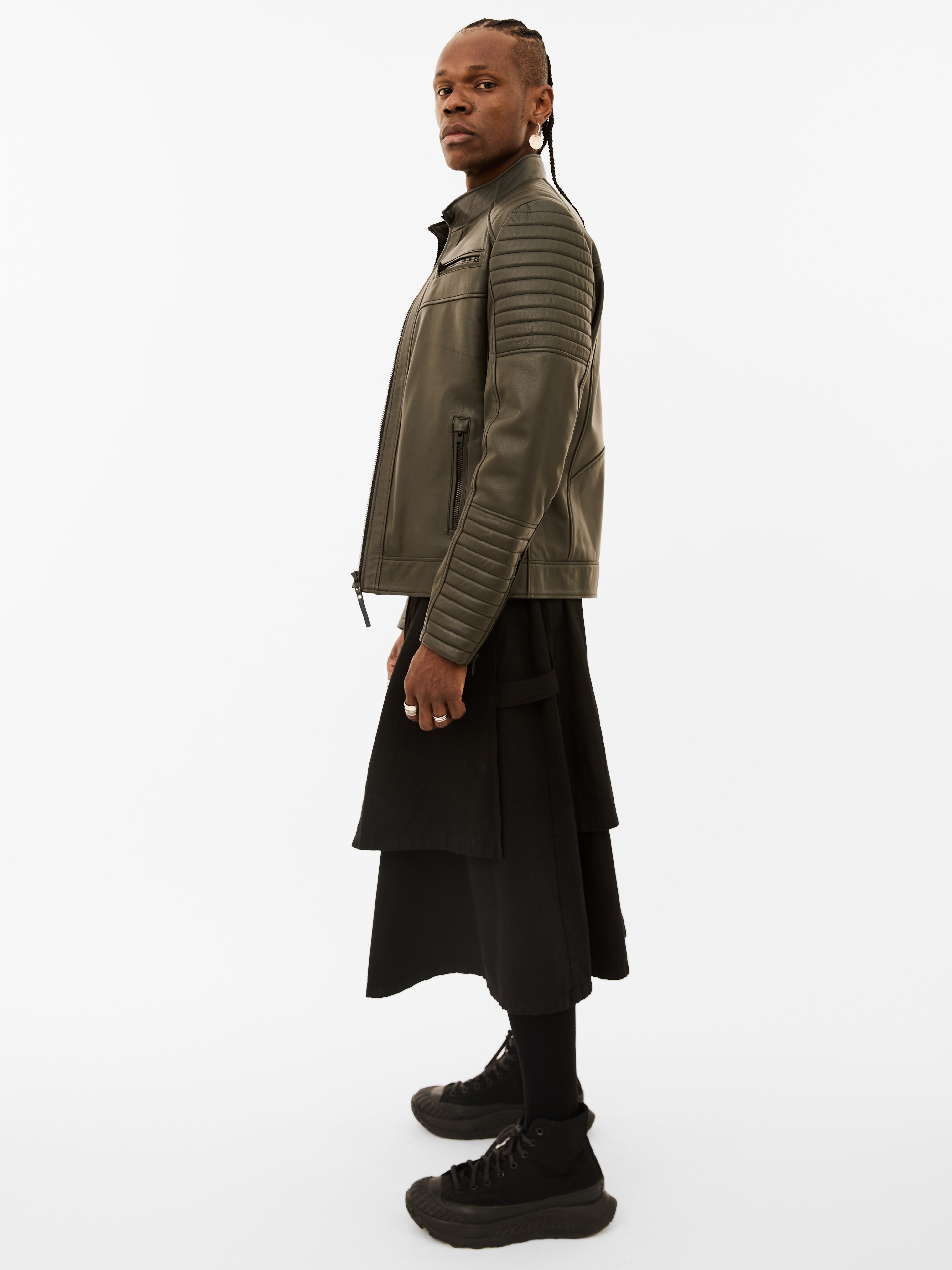 Person wearing a green quilted leather jacket and black skirt on a white background