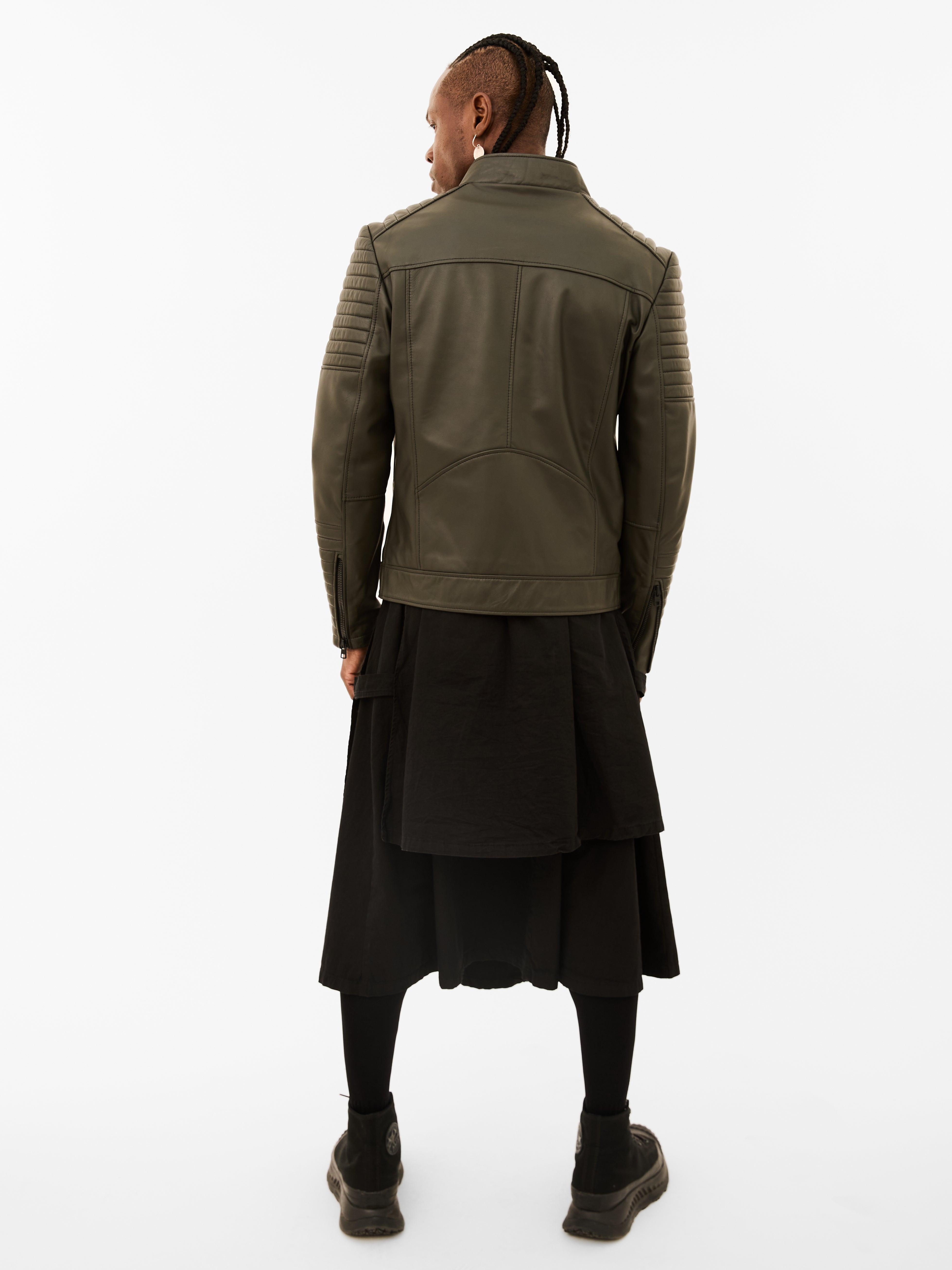 Person wearing a green leather jacket and black skirt on a white background
