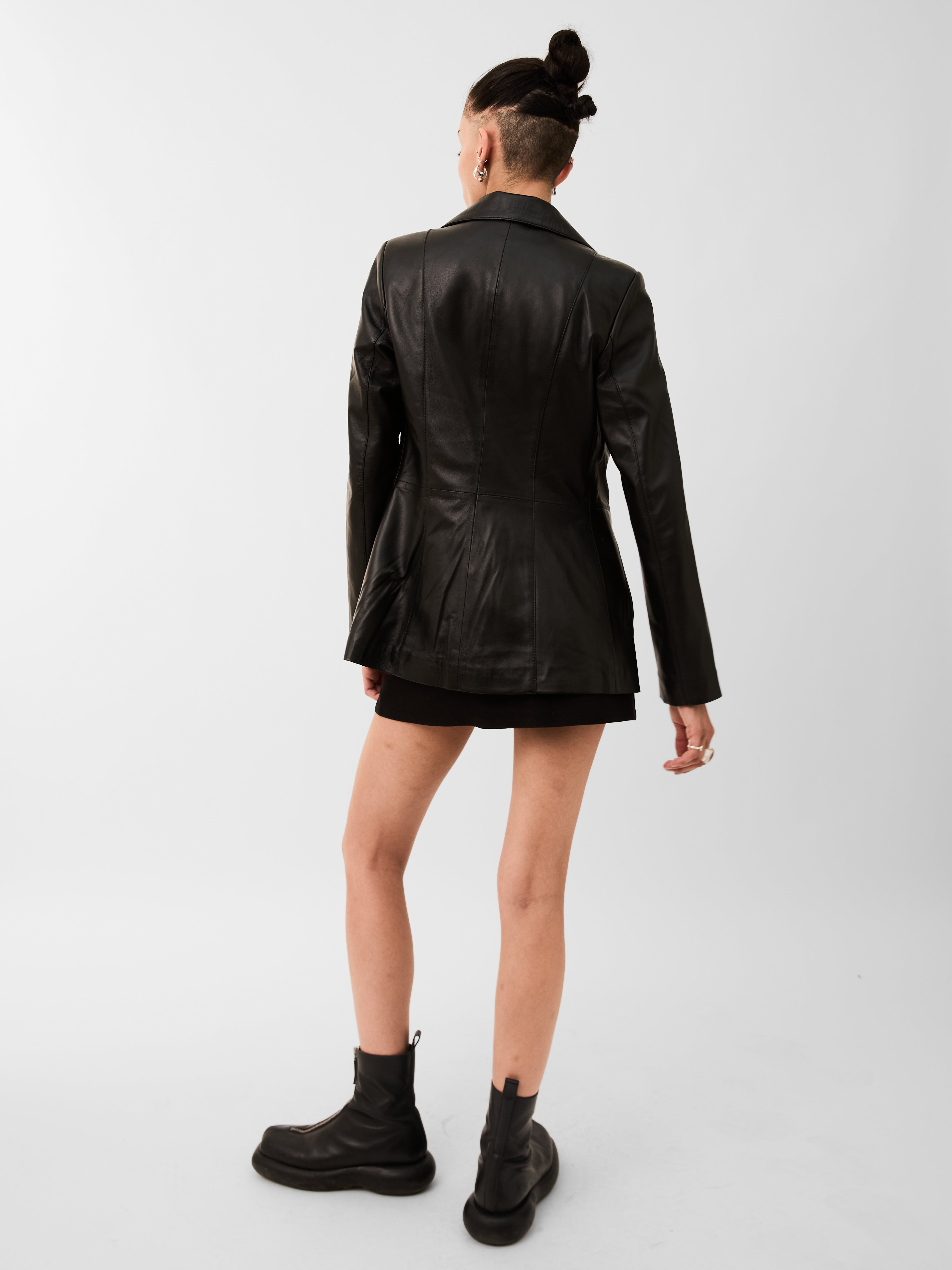 A woman wearing a leather blazer jacket and skirt on a white background