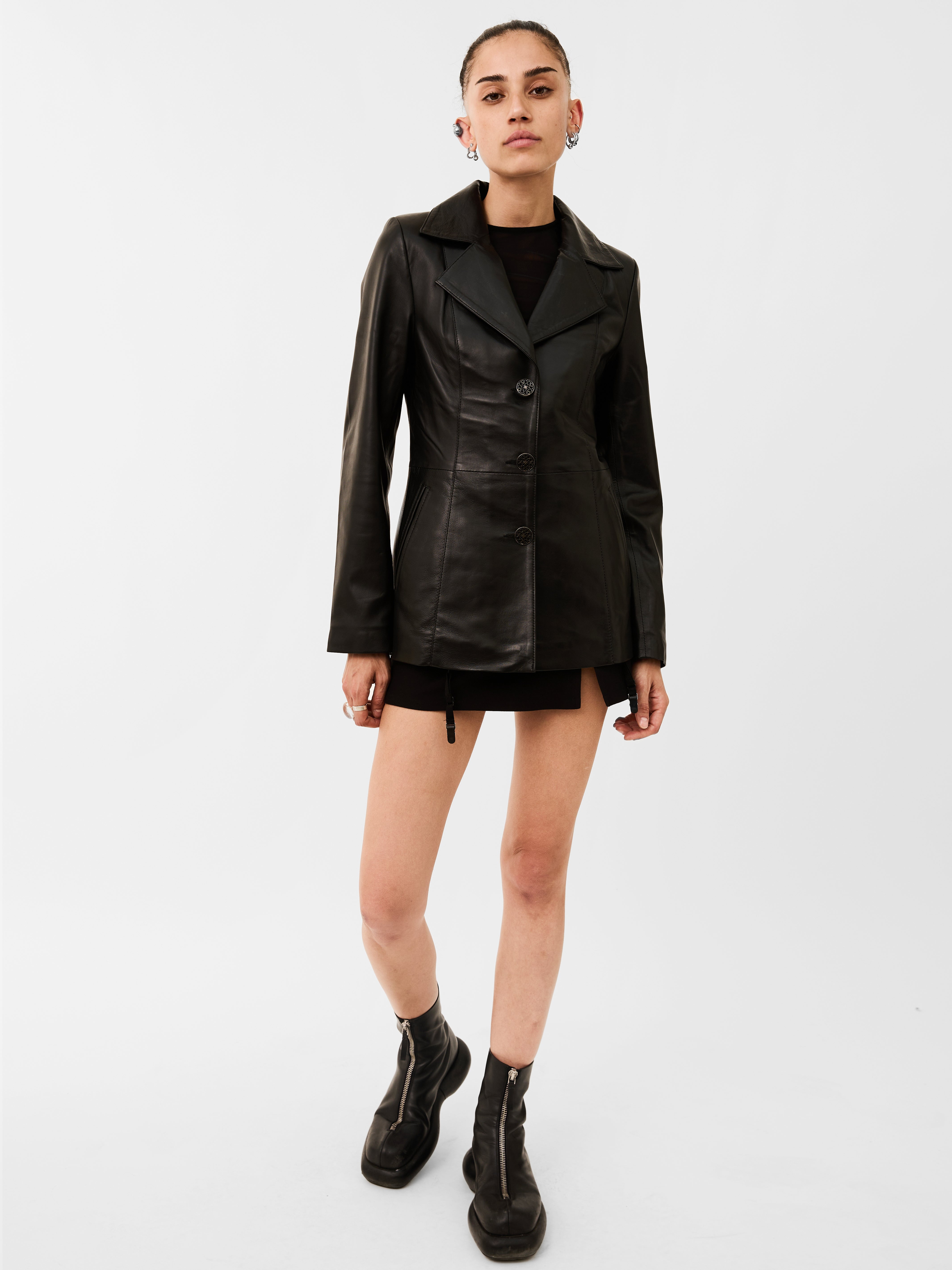 Person wearing a black leather blazer jacket and skirt set on a white background