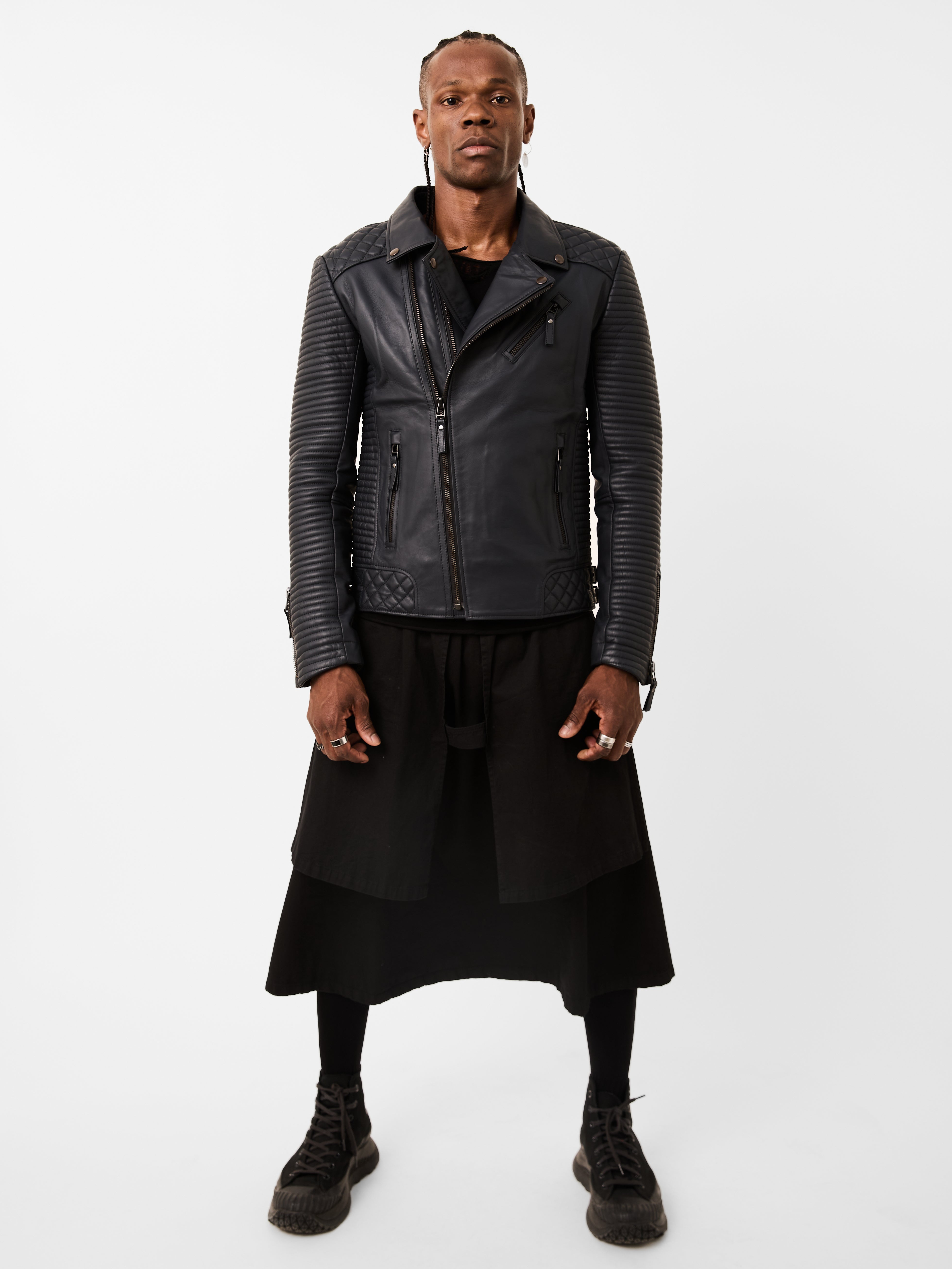 Man wearing a navy blue leather biker jacket and black skirt on a white background