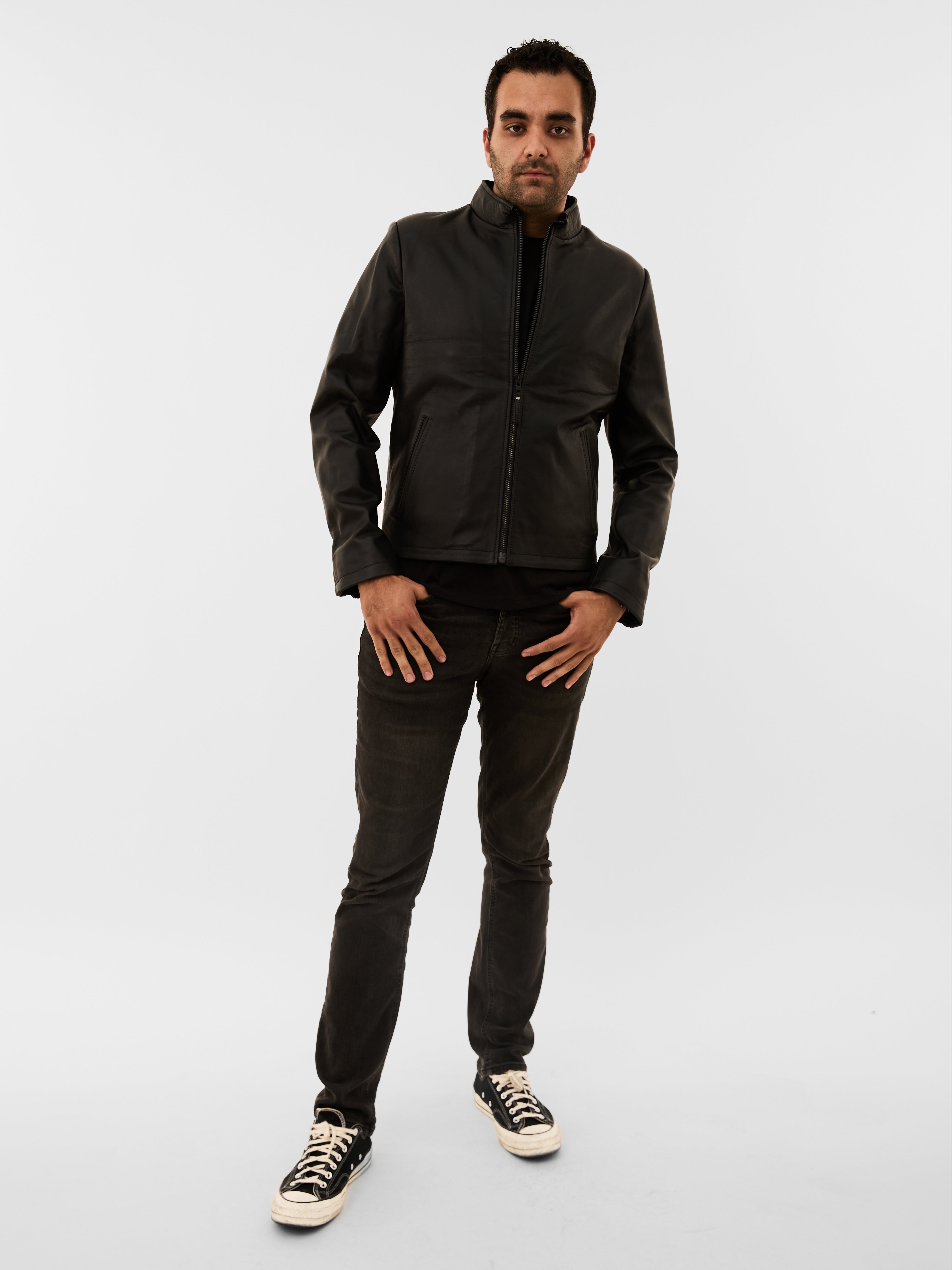 Man wearing a black jacket, black pants, and black shoes on a white background