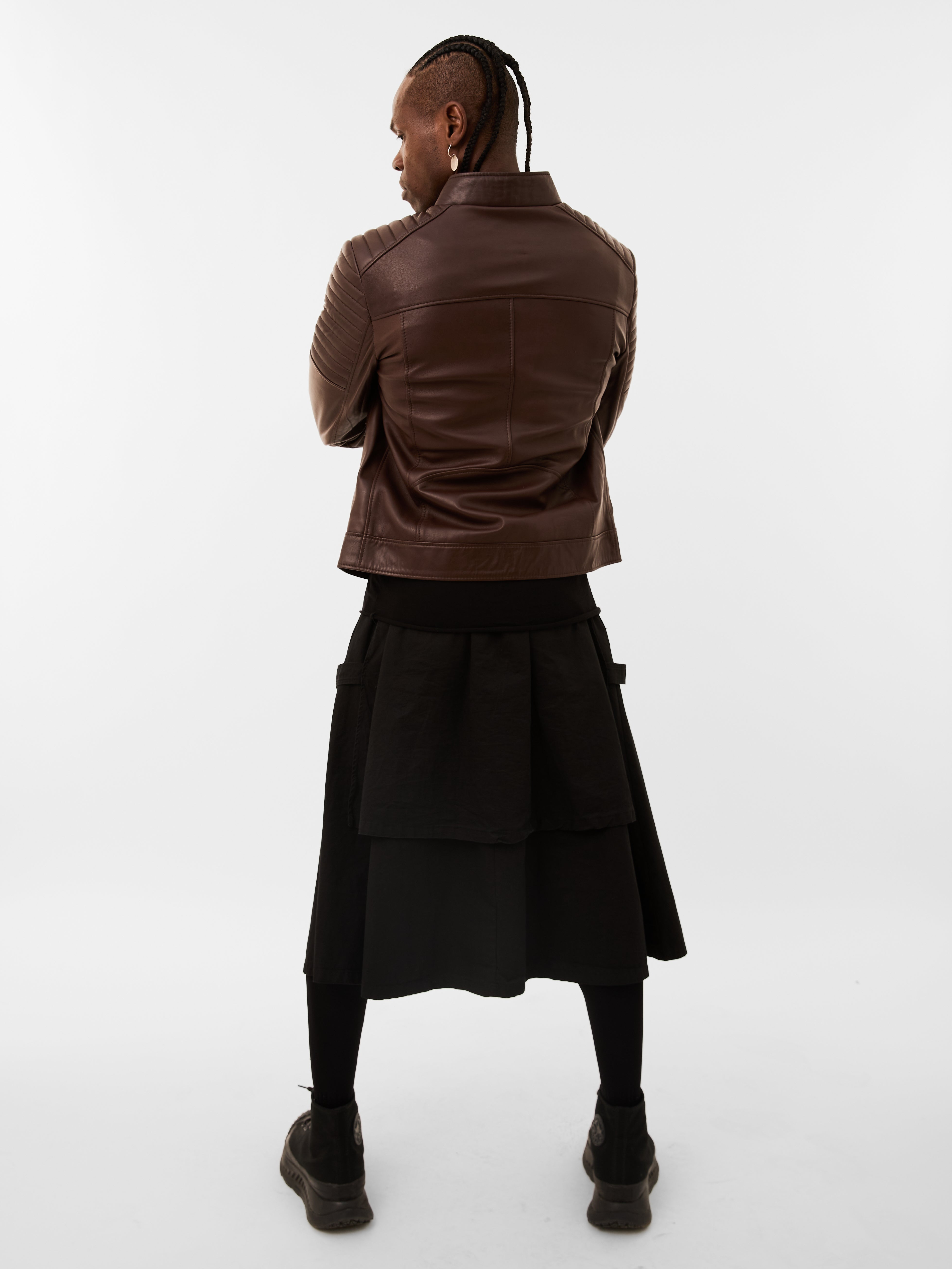 Person wearing a brown leather jacket and black skirt on a white background