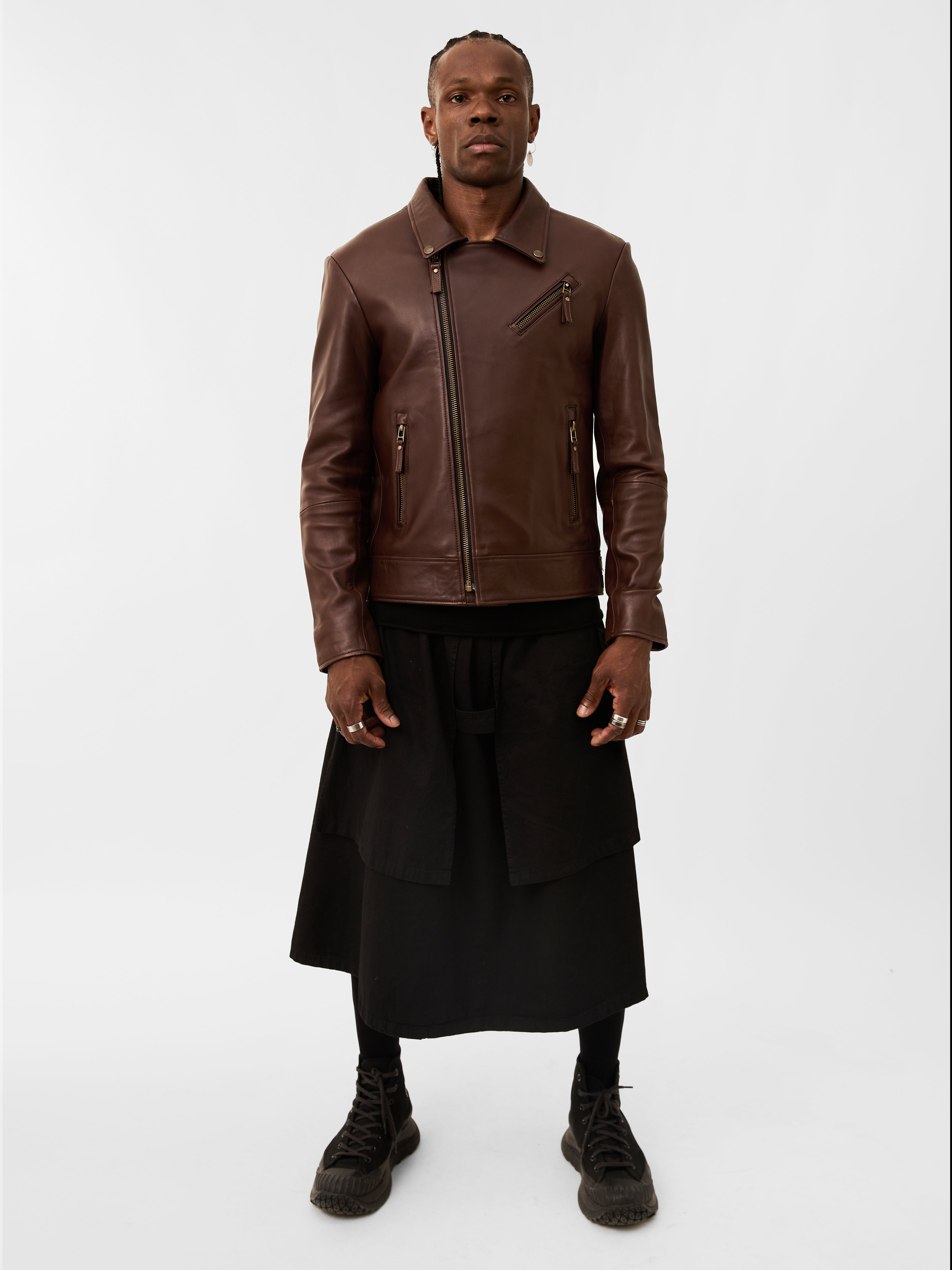 Person wearing a brown leather jacket and black skirt on a white background