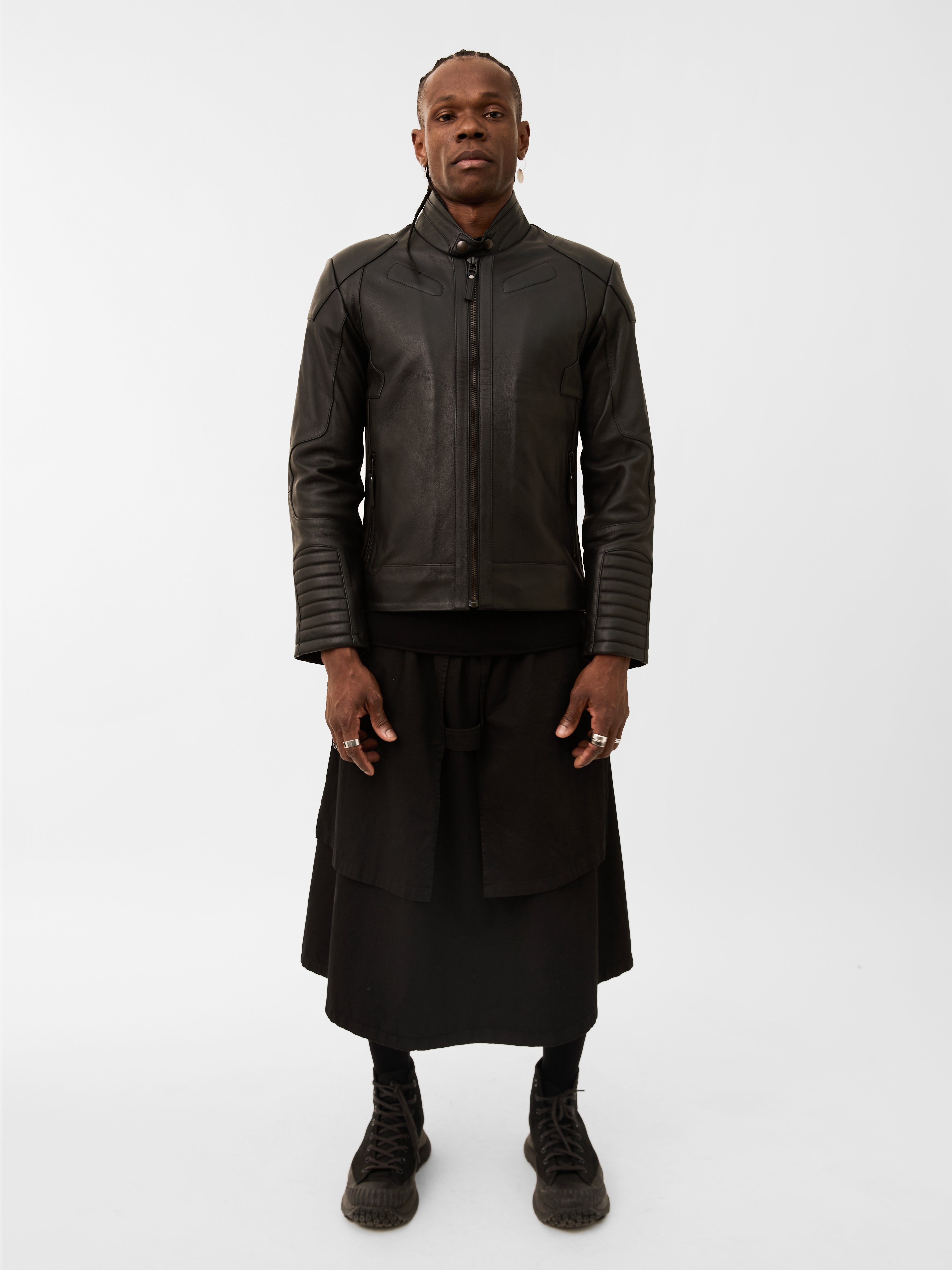 Person wearing a dark leather biker jacket and black outfit on a white background