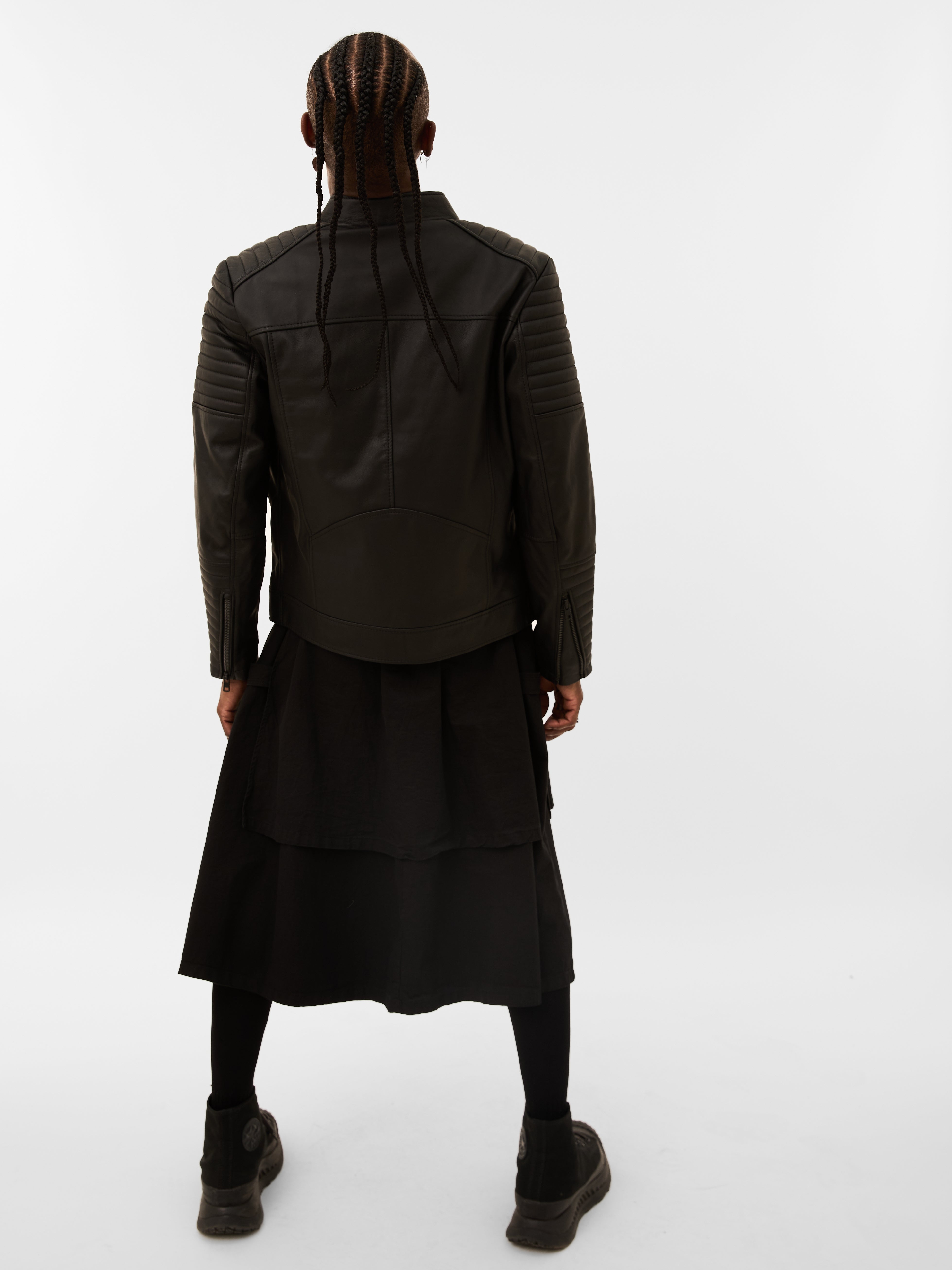 Person wearing a black quilted leather jacket and skirt set on a white background