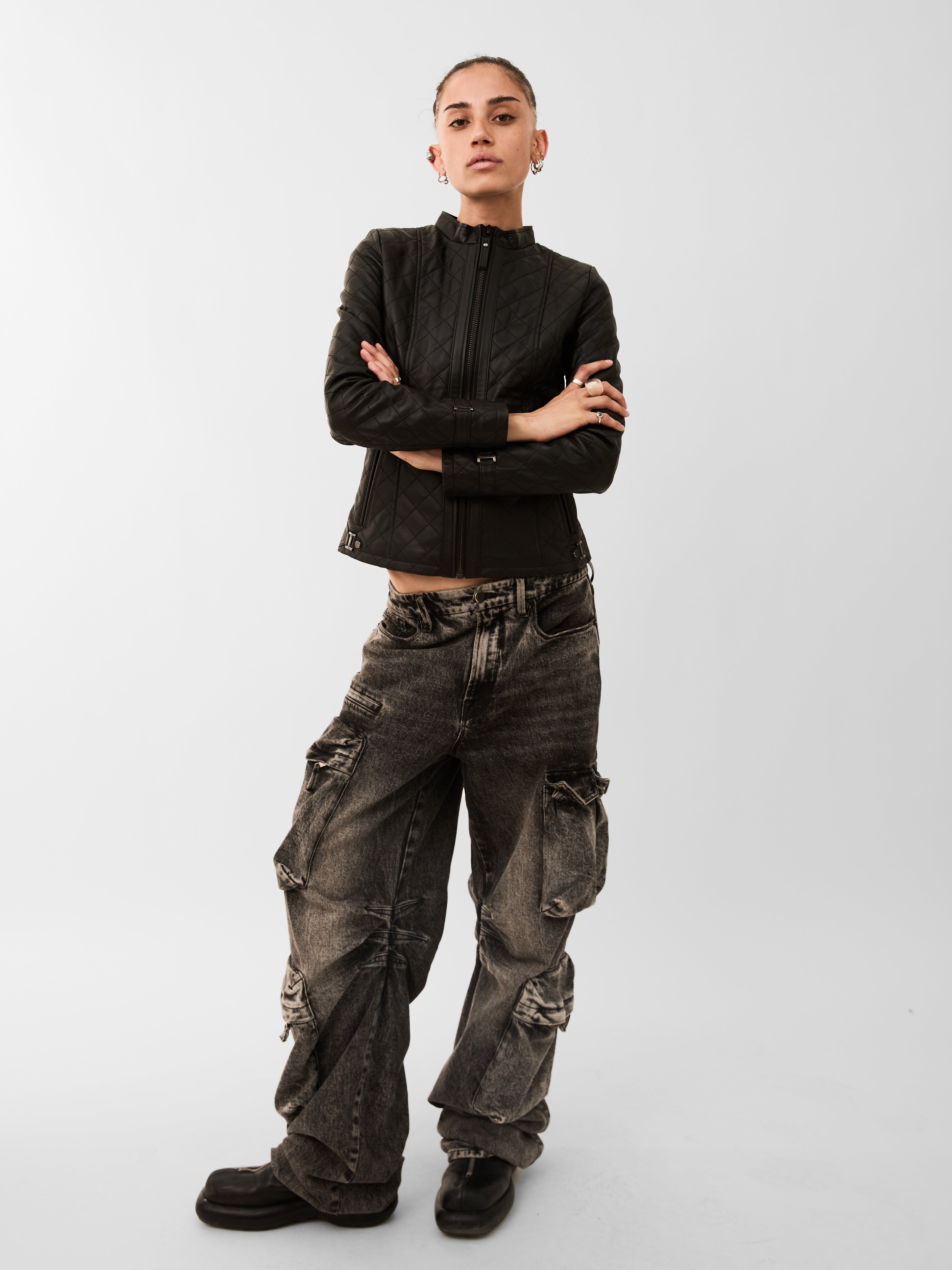 Person wearing a black jacket and distressed cargo pants on a white background