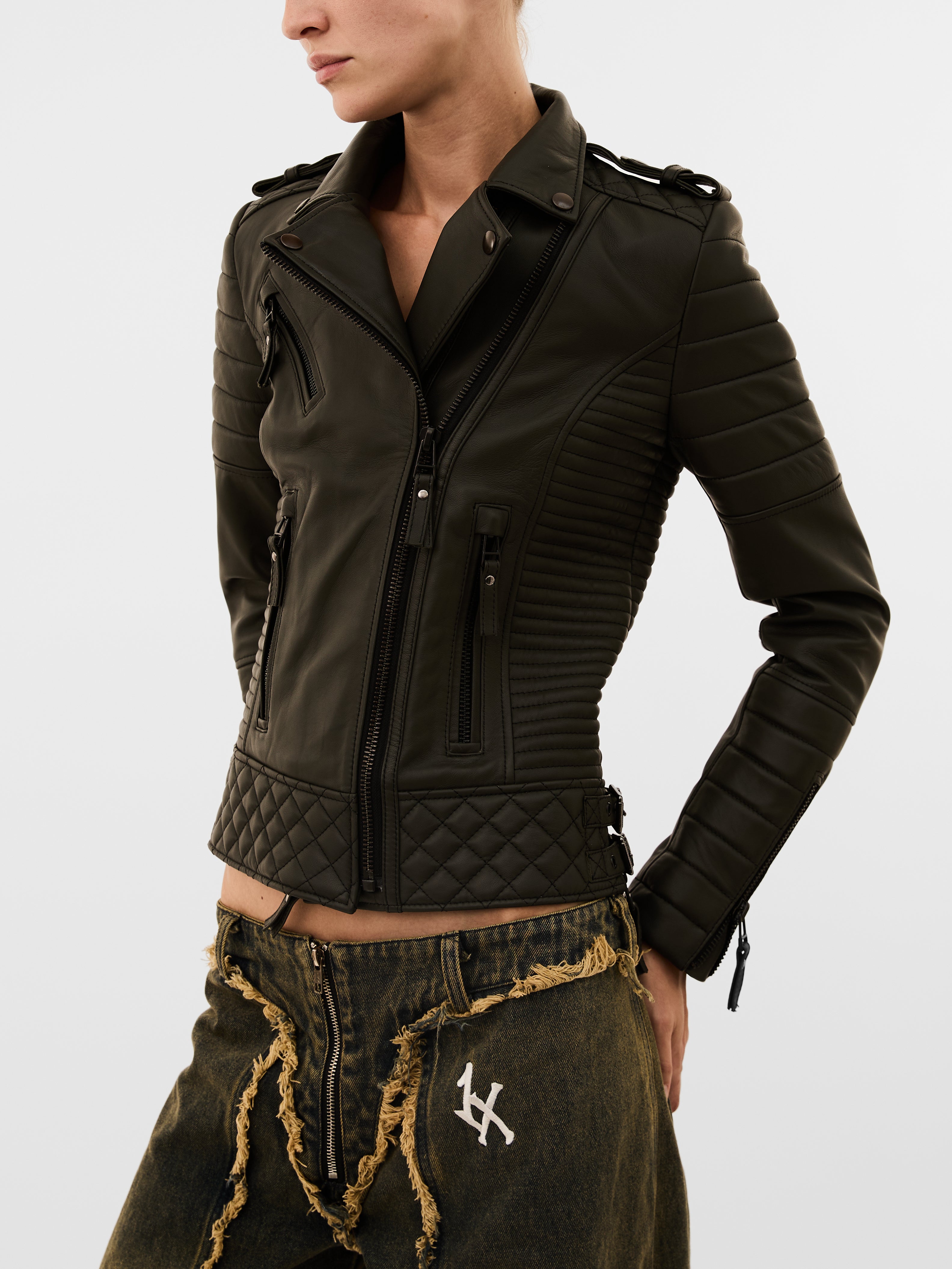 Person wearing a dark green quilted jacket with a white logo on pants against a light gray background