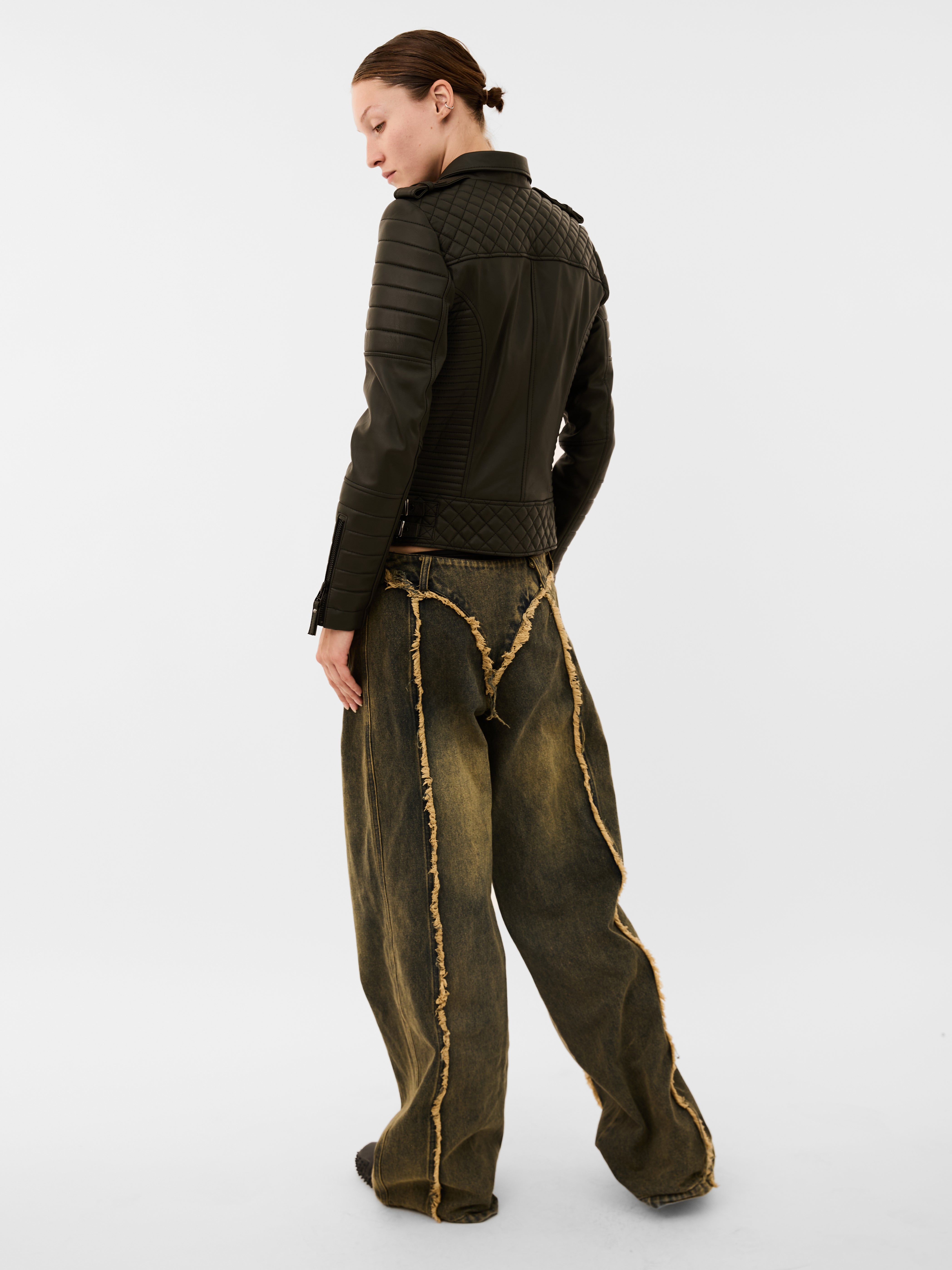 Person wearing a dark green jacket and wide-leg pants with gold accents on a white background