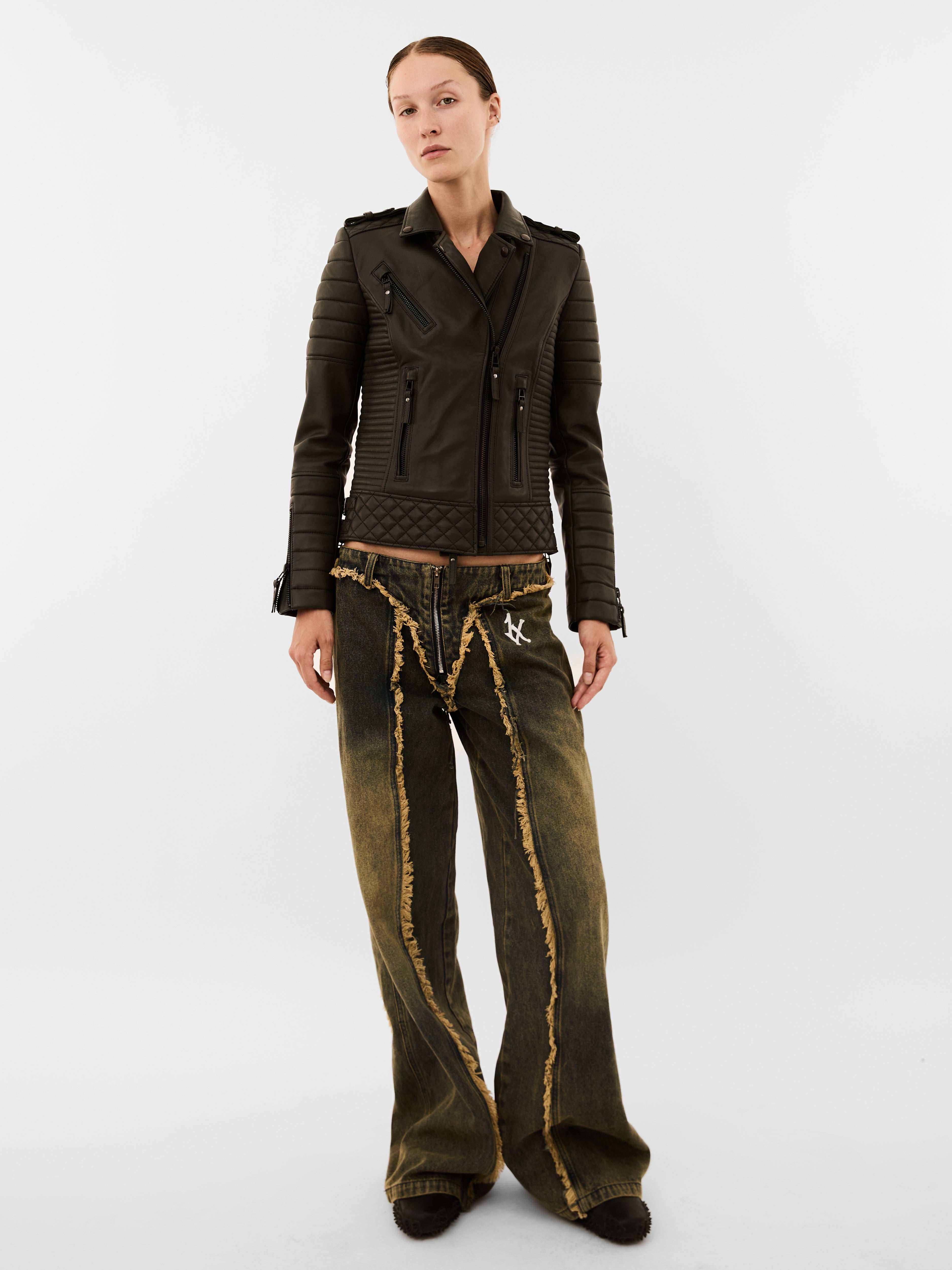 Person wearing a dark green jacket and distressed jeans on a white background