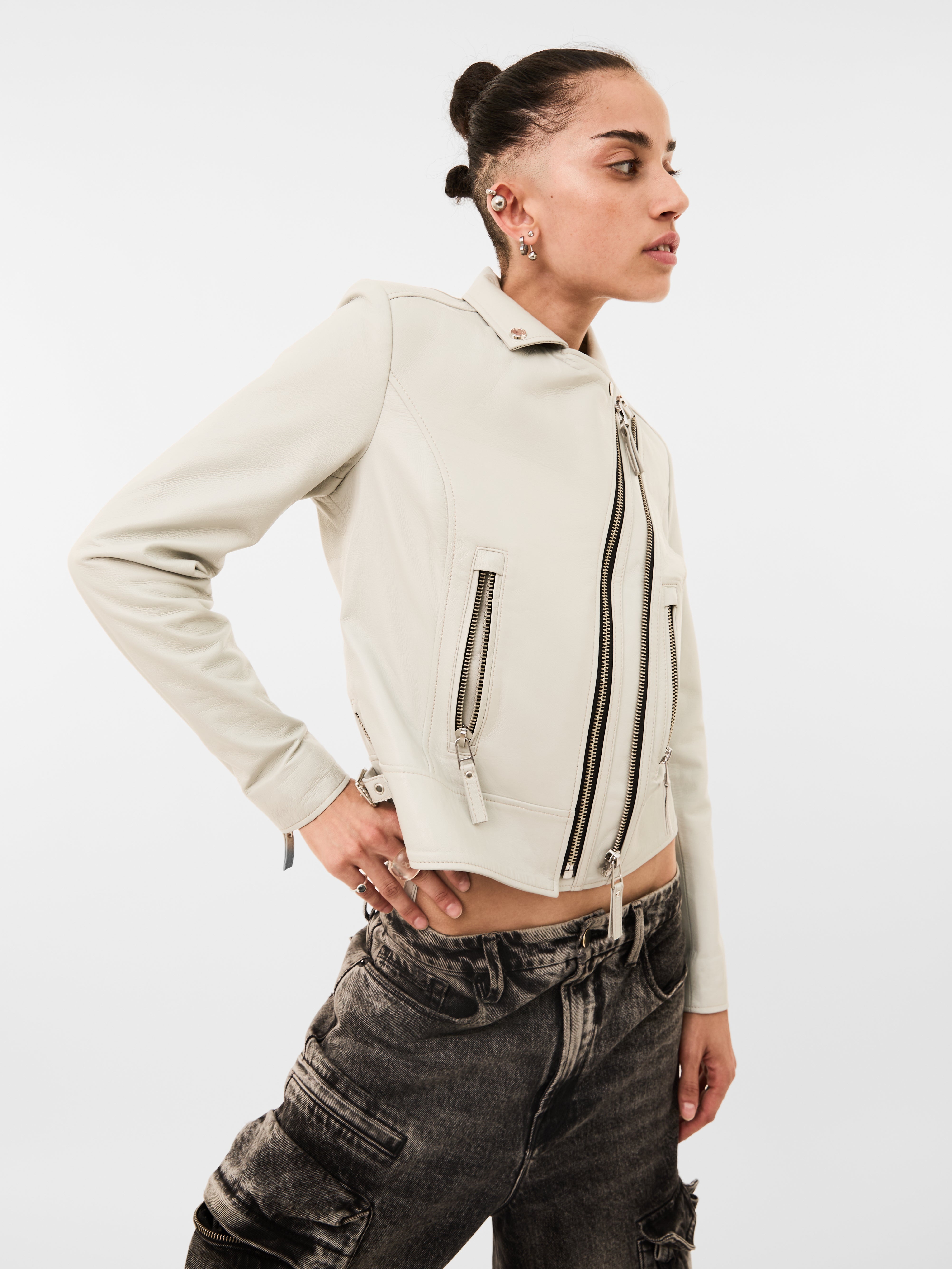 Person wearing a beige leather biker jacket with zippers on a white background