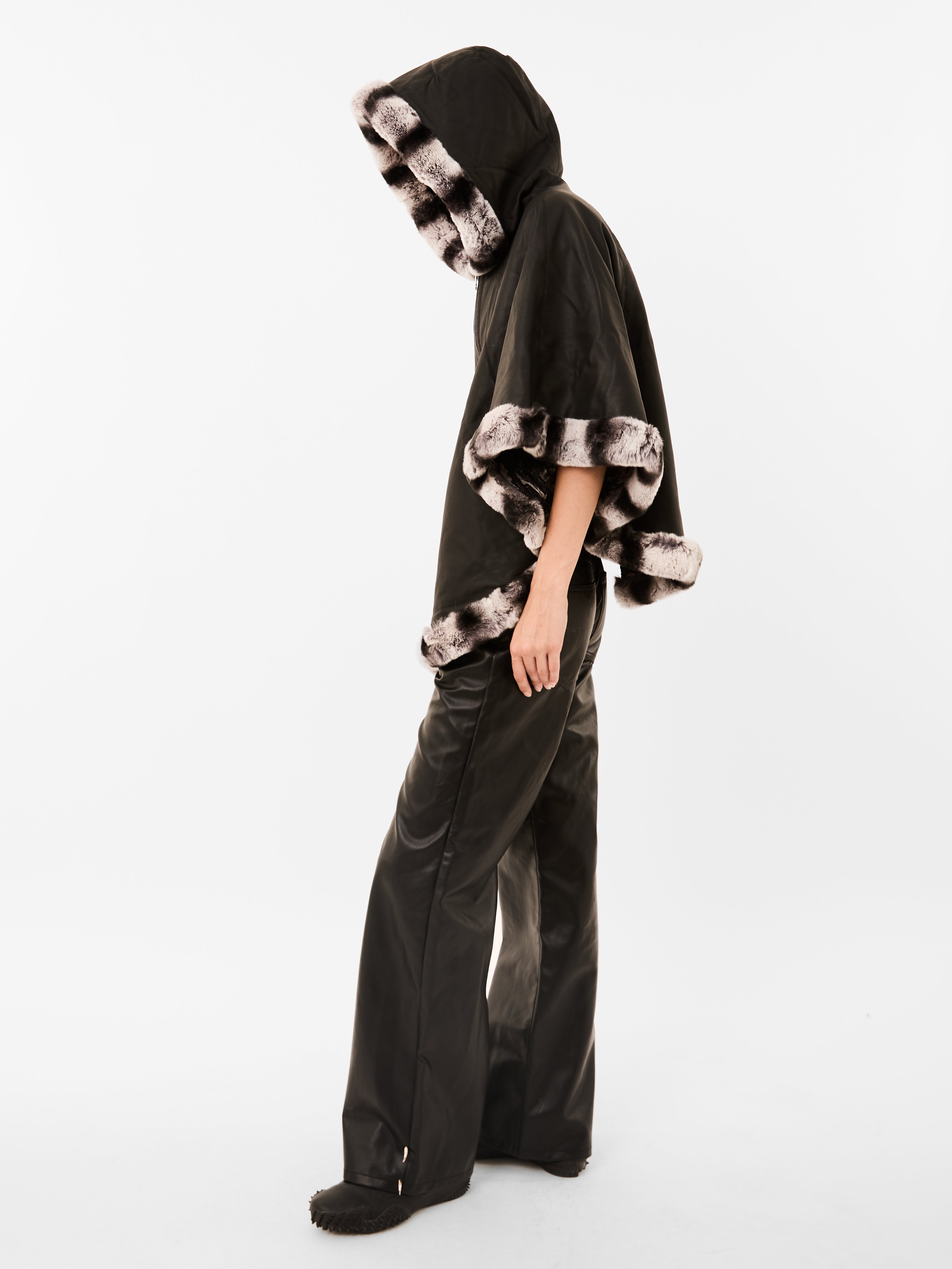 Side look of women wearing a black pancho with fur trim on a white background