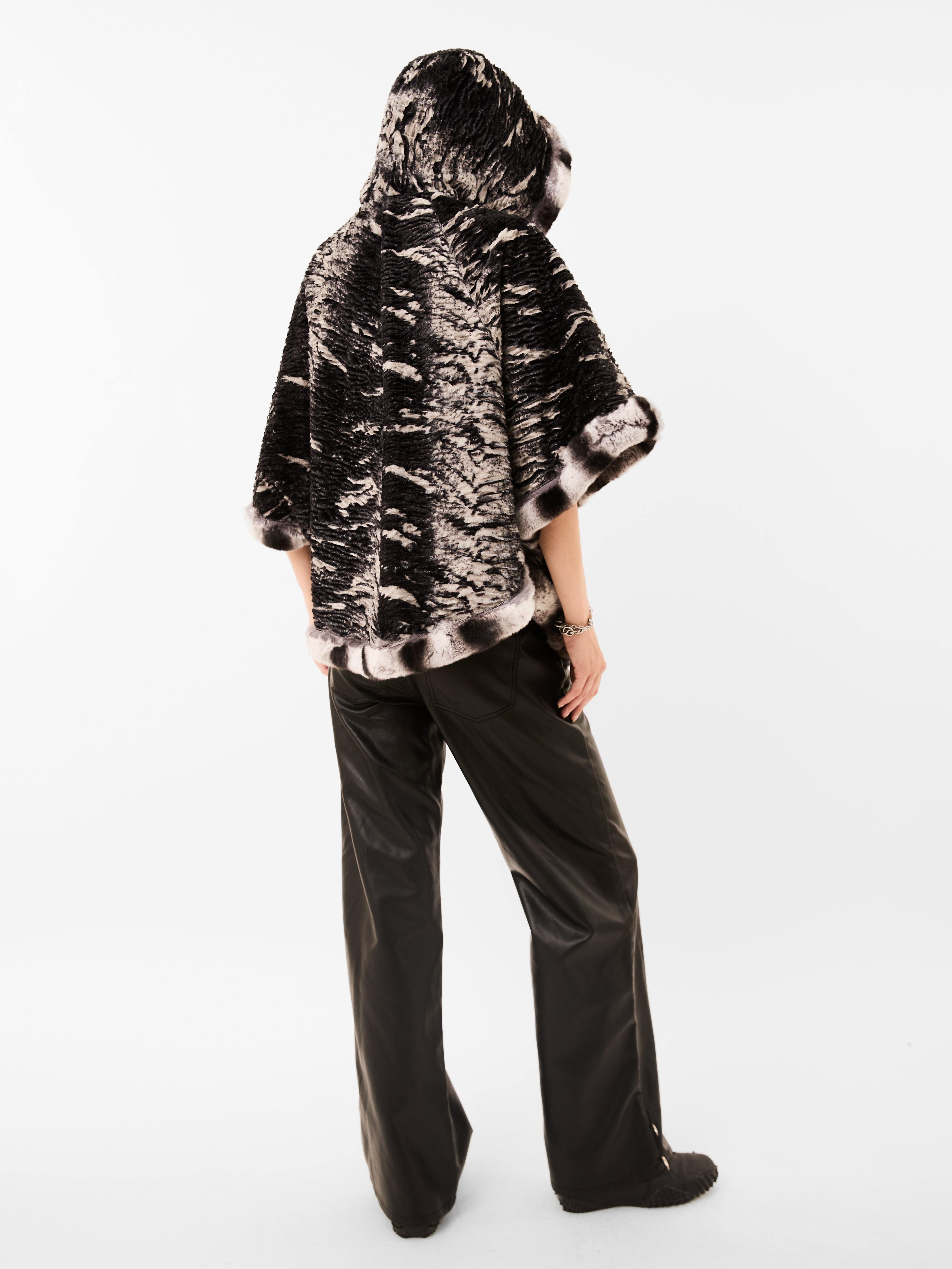 Person wearing a black and white patterned fur pancho and black pants on a white background