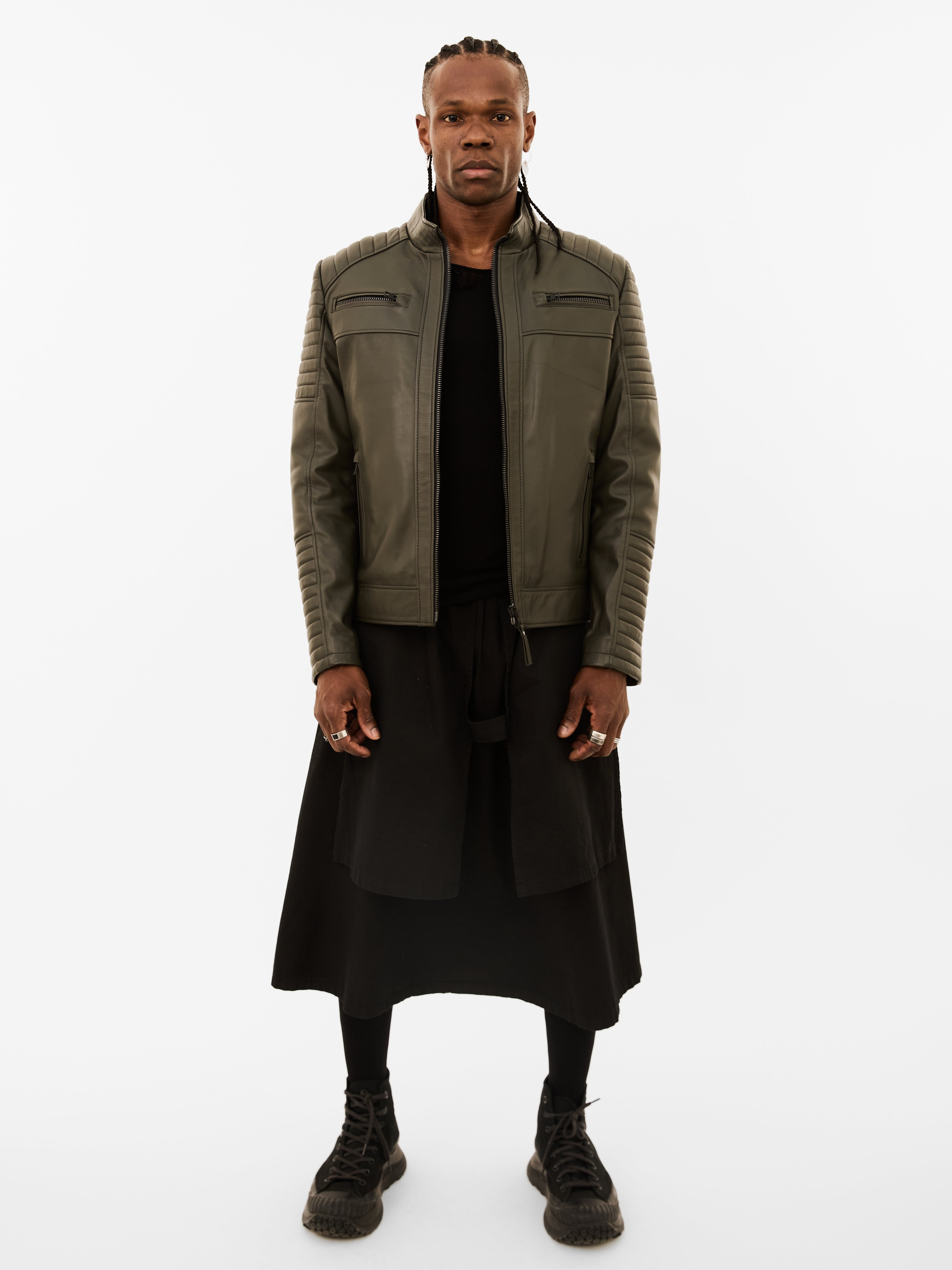 Person wearing a green leather biker jacket and black outfit on a white background