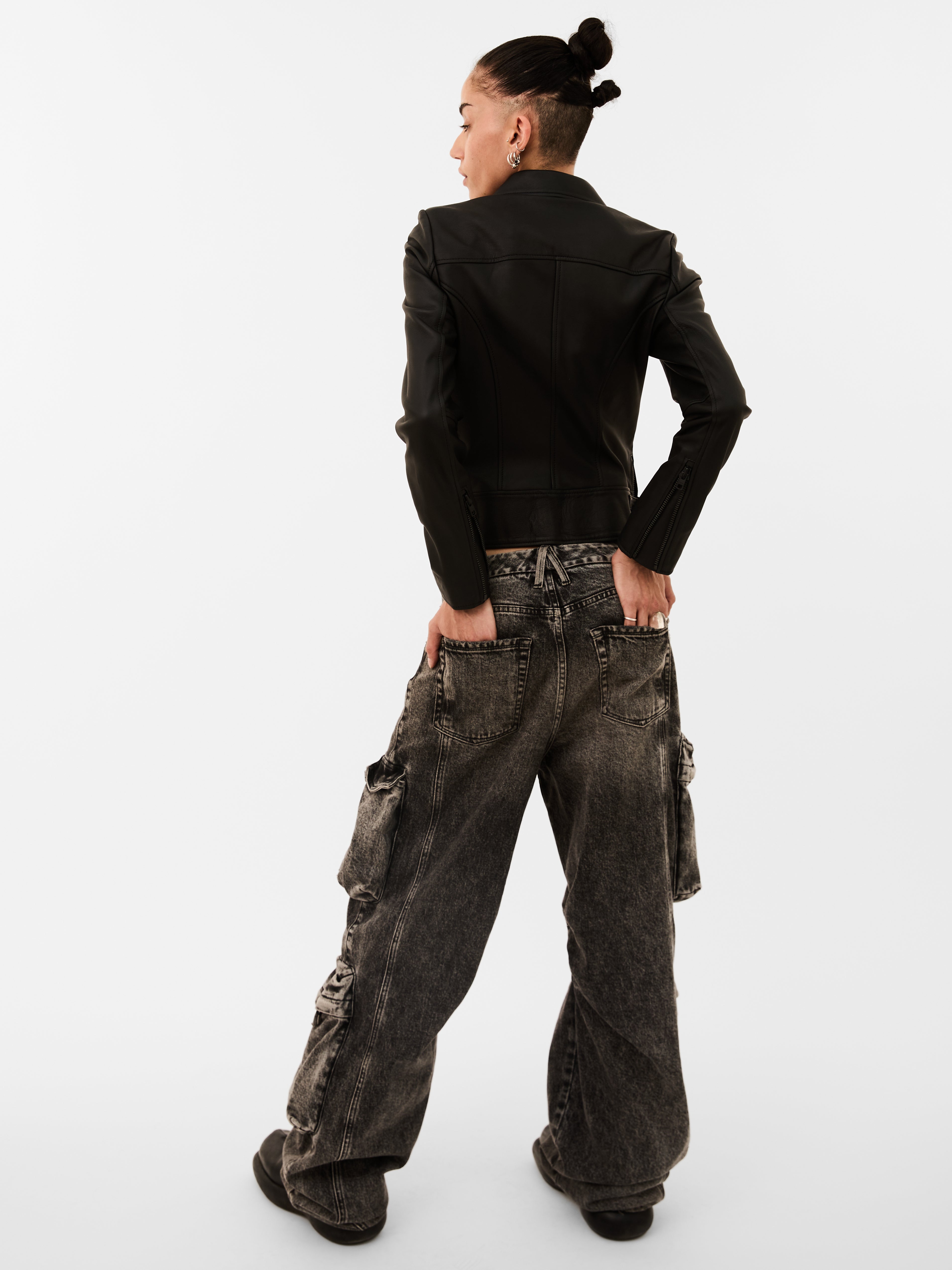 Person wearing a black leather biker jacket and dark cargo pants on a white background
