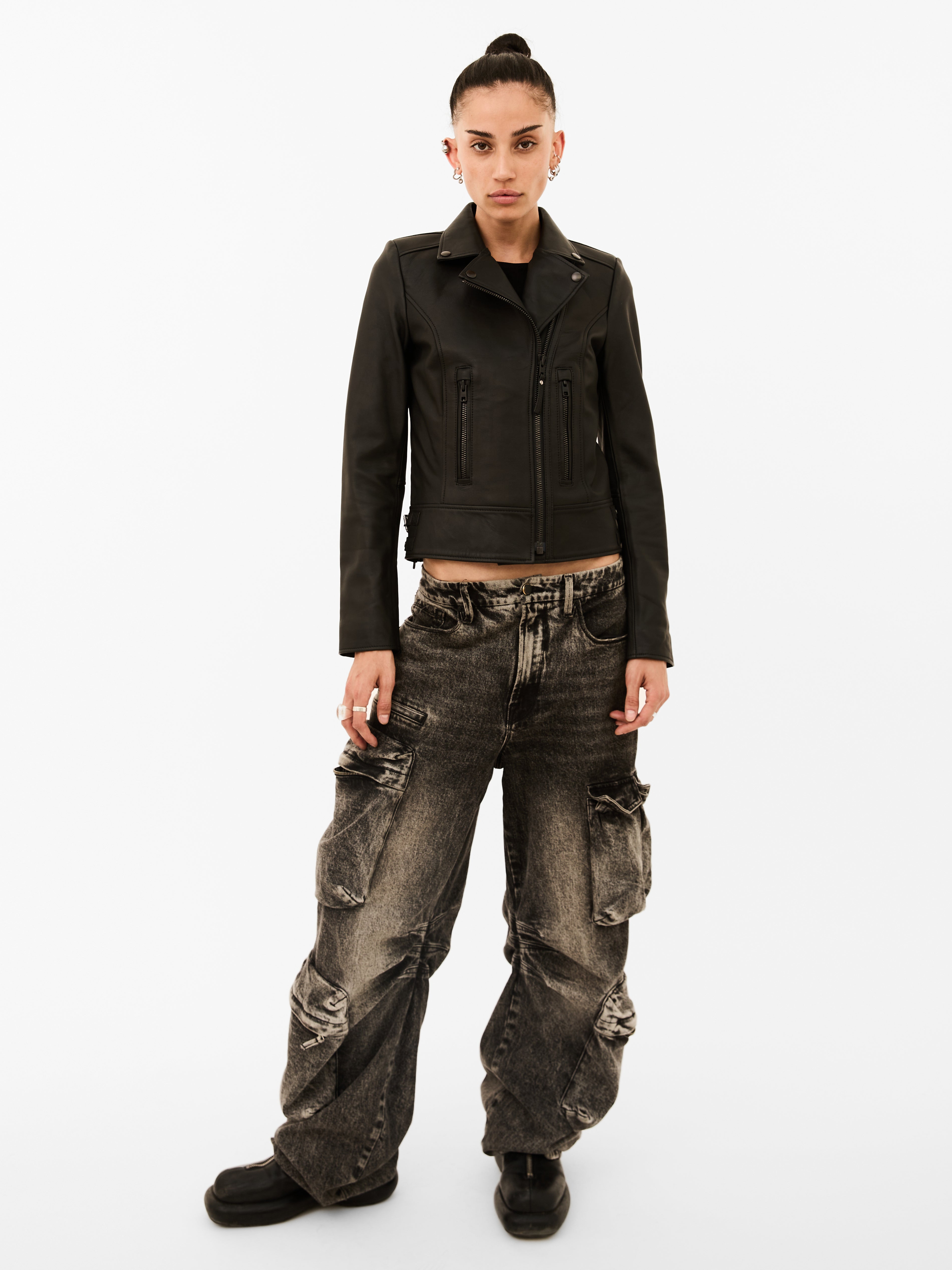 Person wearing a black biker jacket and distressed jeans on a white background