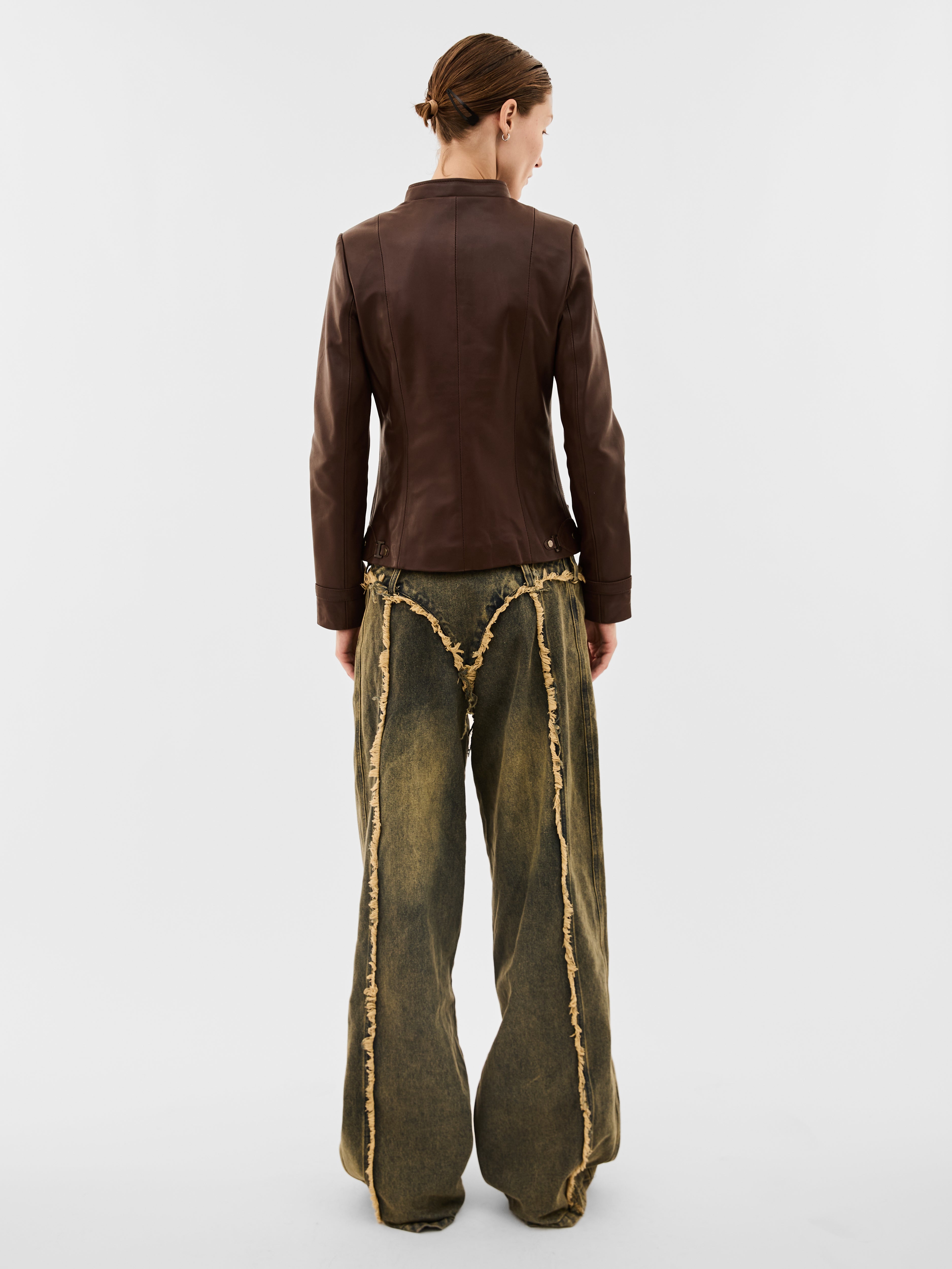 A woman wearing a brown leather jacket and green jeans with gold trim on a white background