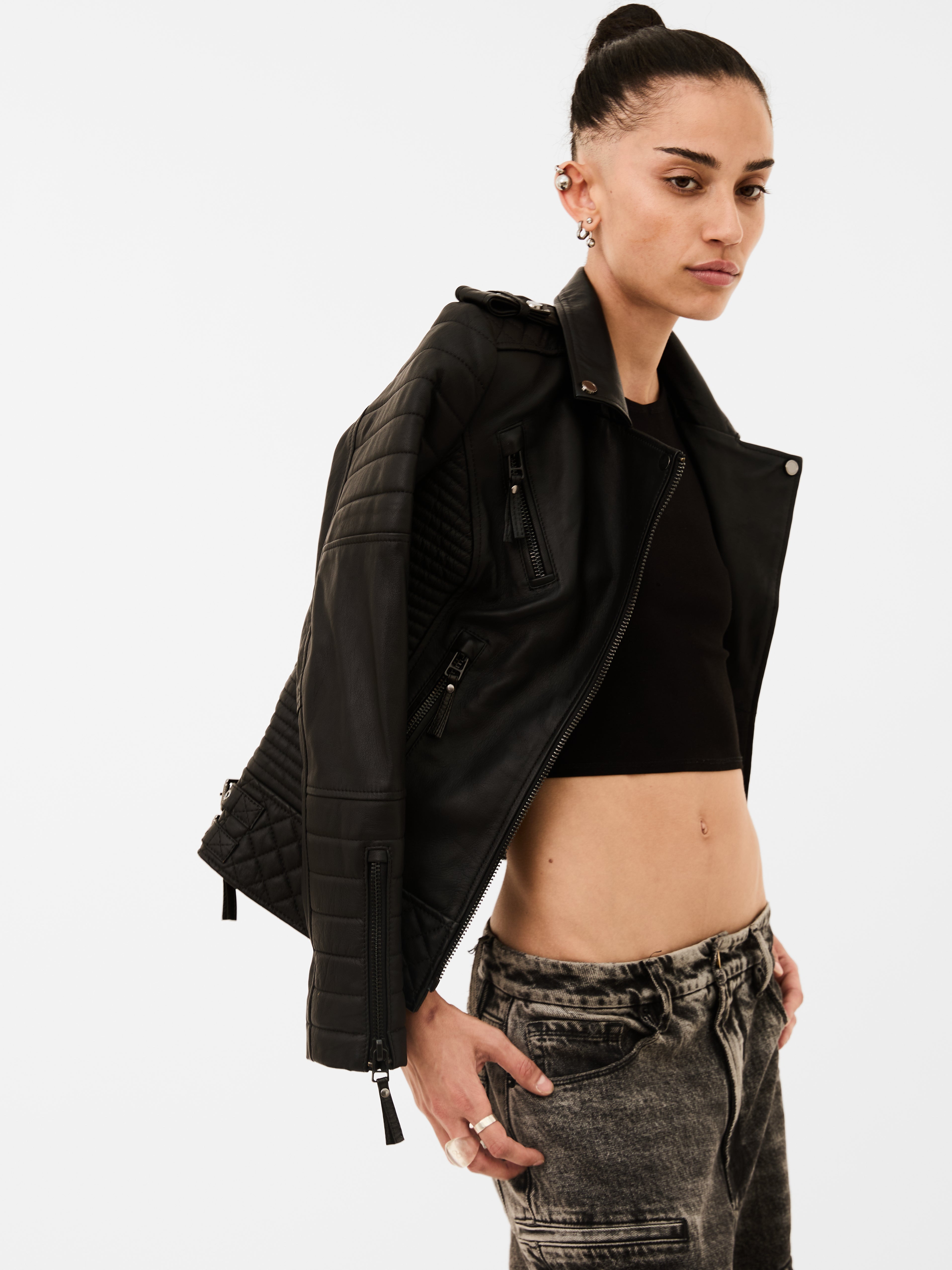 Person wearing a black leather jacket and gray pants on a white background
